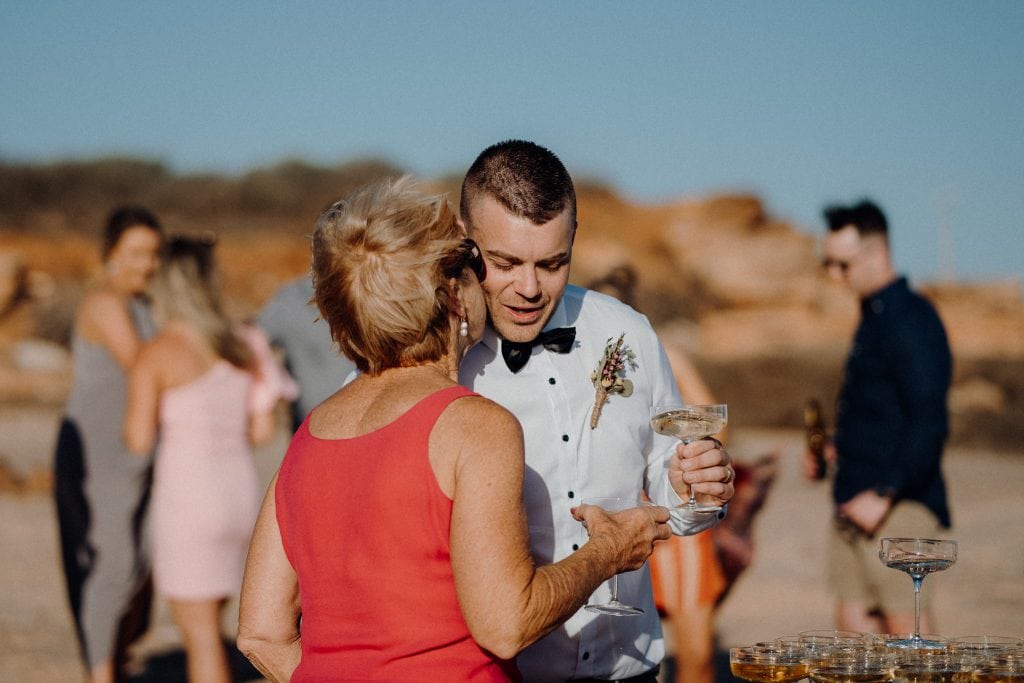 older woman in red dress giving groom a kiss on the cheek