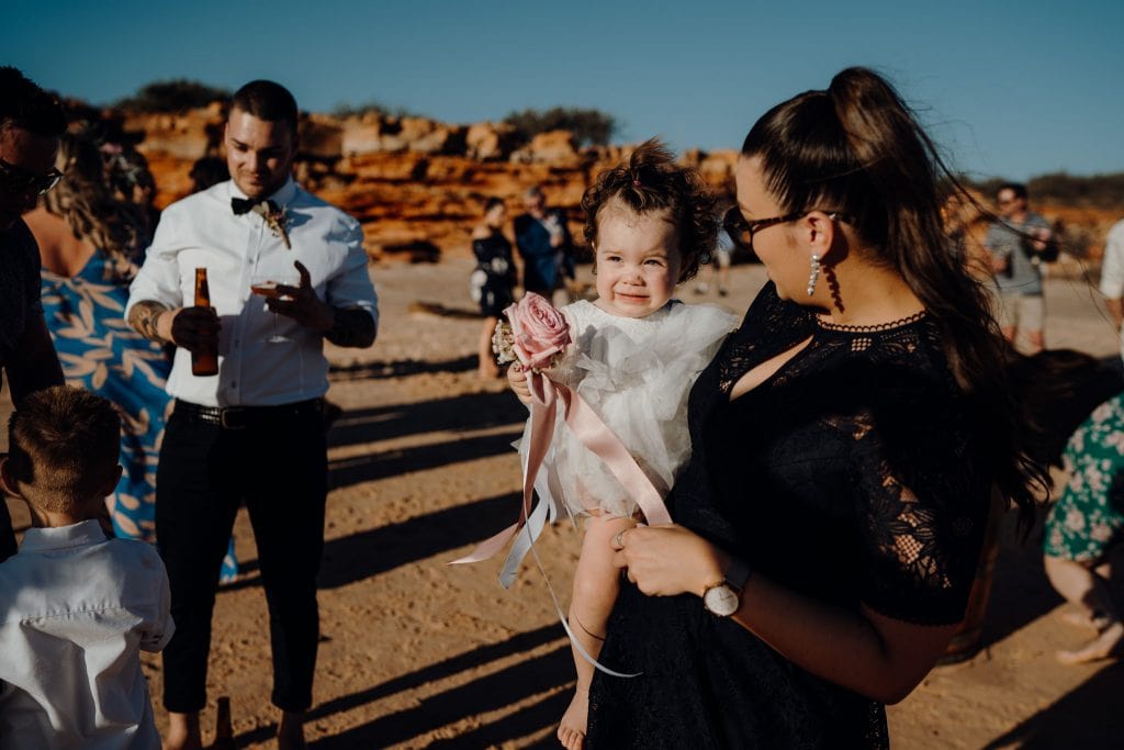 little girl in white dress in the arms of a woman at relaxed beach wedding