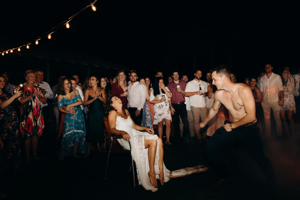 groom stripped off his shirt and dances around his bride who is sitting on a chair under the stars
