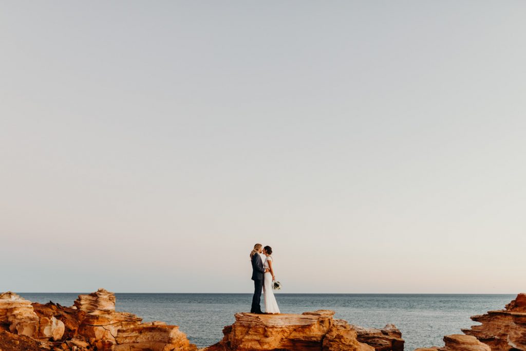 wedding couple standing on red cliff top in Broome kissing 