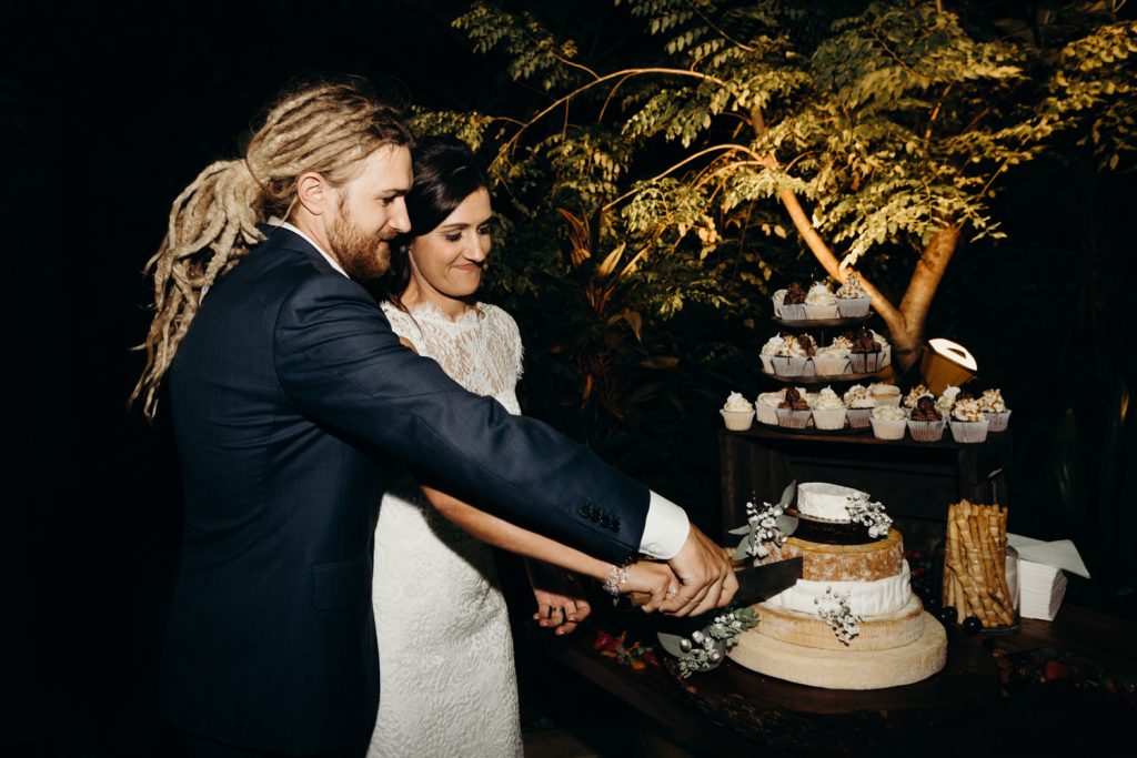 wedding couple cutting wedding cake which is a cheese wheel 