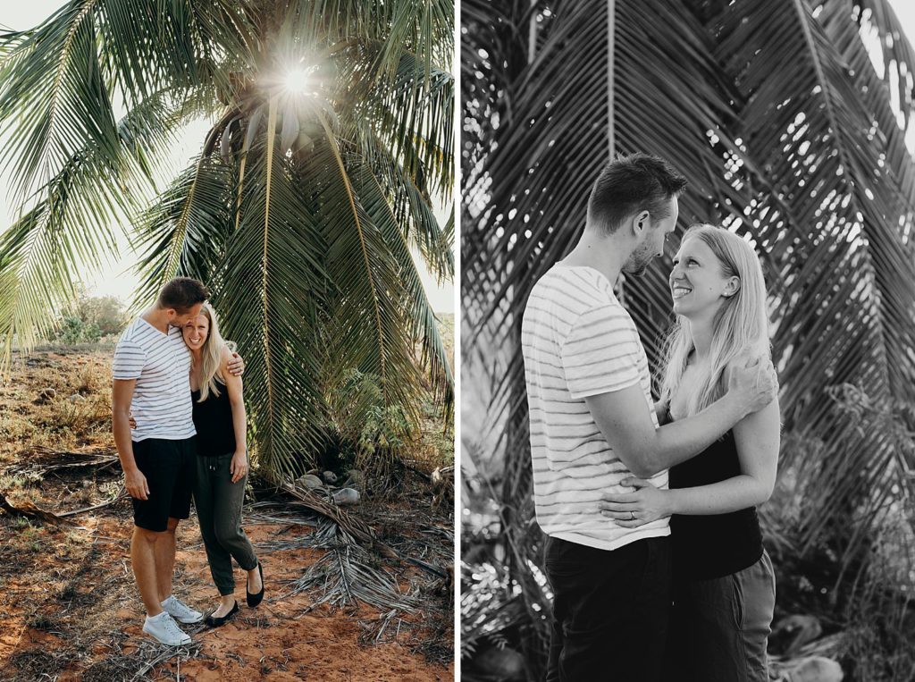 young engaged couple standing in front of a palm tree with the sun peaking through