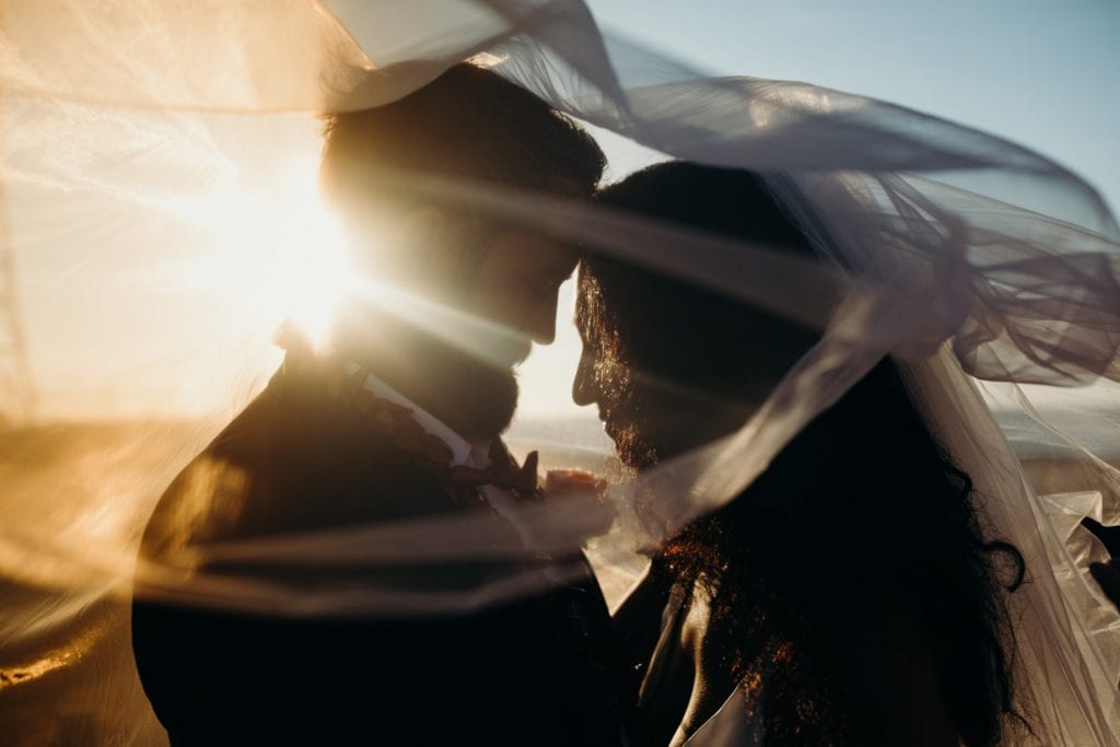two people under a large veil with sunlight beaming from behind