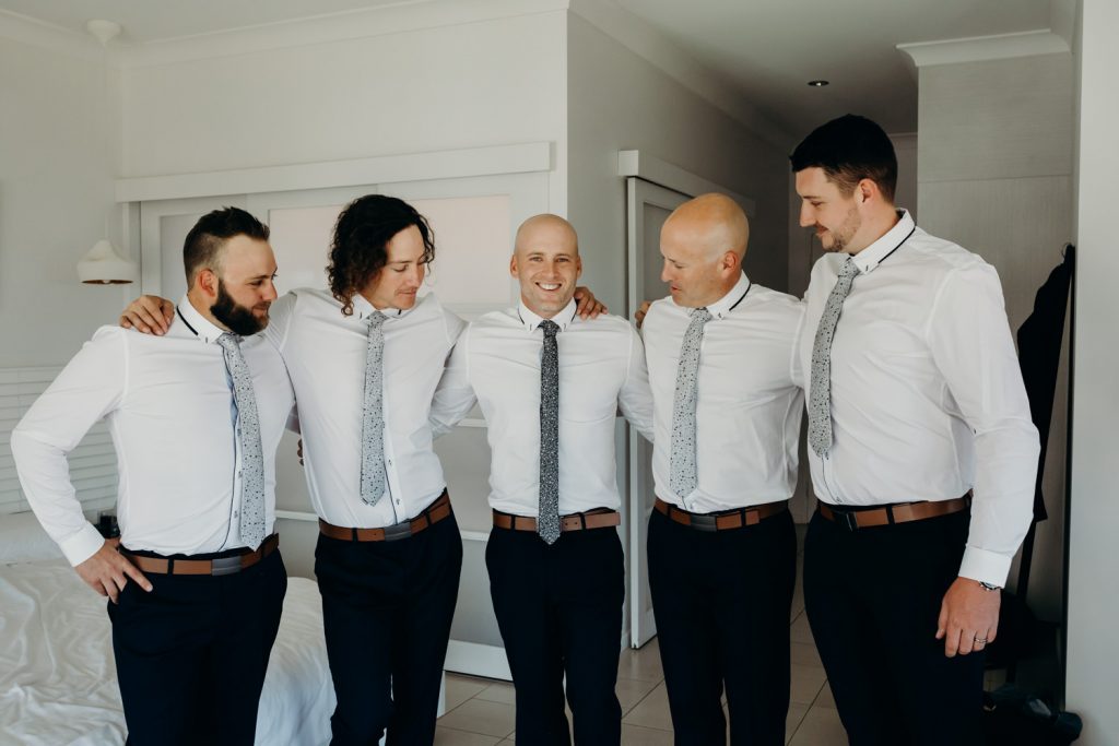 groom with groomsmen standing in half circle in hotel room