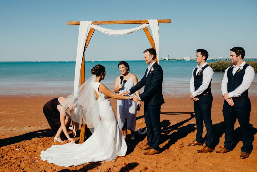 bride and groom holding hands under a wooden arbour with celebrant 