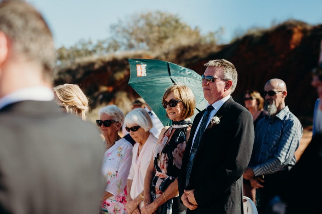 parents of the groom are looking on at son's beach ceremony