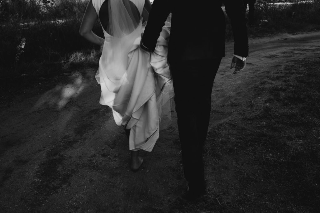 black and white shot of wedding couple walking with groom holding dress up