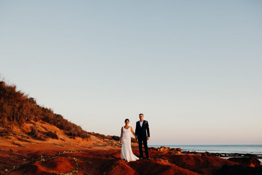 couple of people in wedding attire standing on red cliff