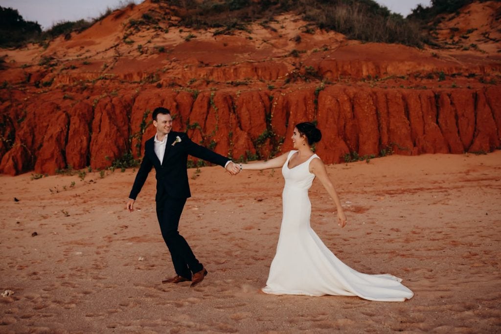 Man in suit dragging bride along on beach