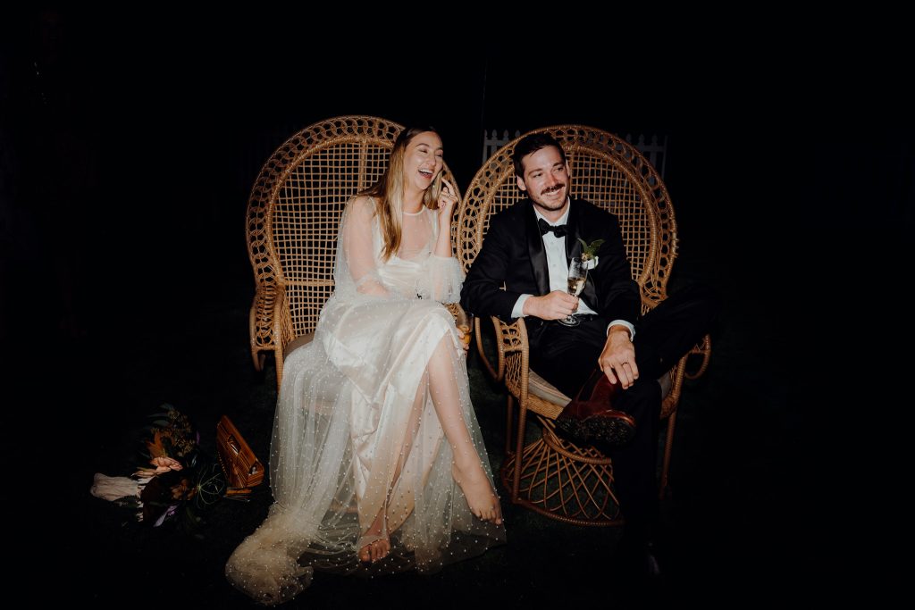 bride and groom sitting in cain chairs during wedding speeches 