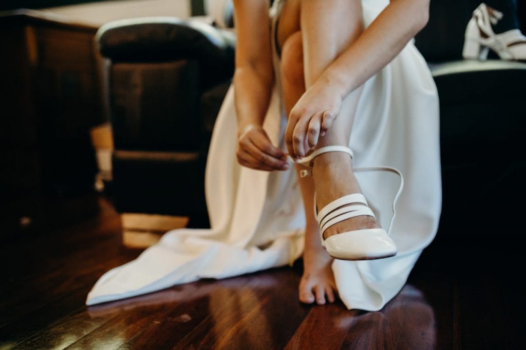 bride is putting on her white wedding shoes