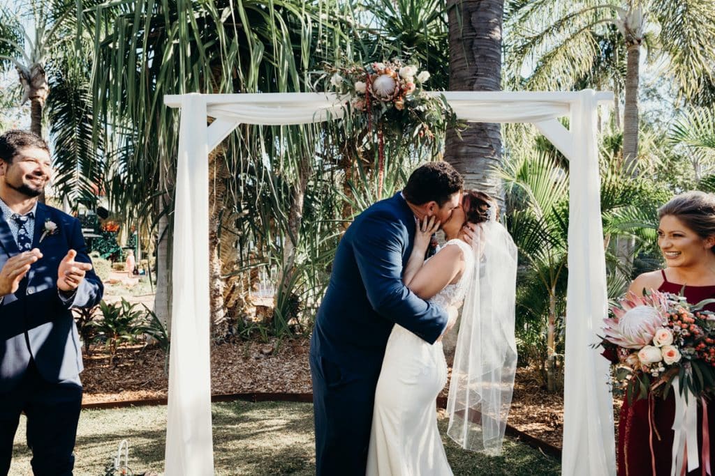 freshly married couple has first kiss under white arbour