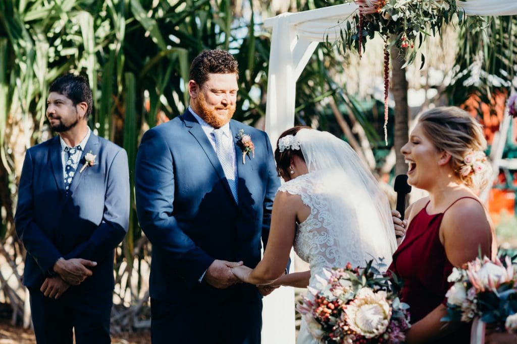 bride and groom smiling under white arbour
