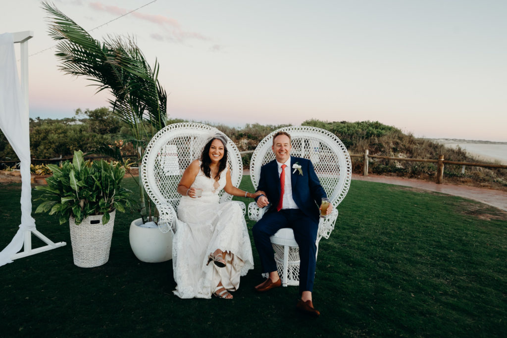 wedding couple sitting in white peacock chairs at Broome surf club in Broome