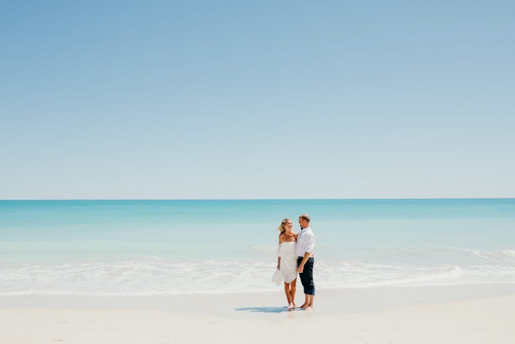 wedding couple standing on the waters edge with blue ocean behind them