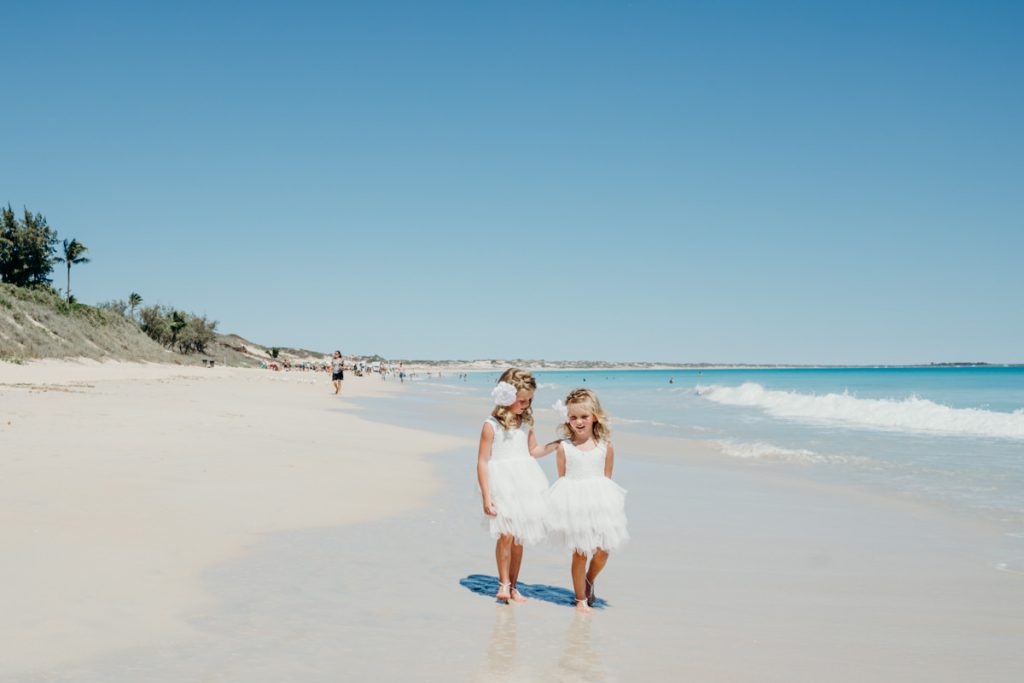 flower girls in white dresses walking along Cable Beach in Broome