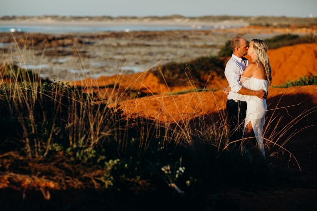 Kissing wedding couple at Gantheaume Point with long grass in the foreground
