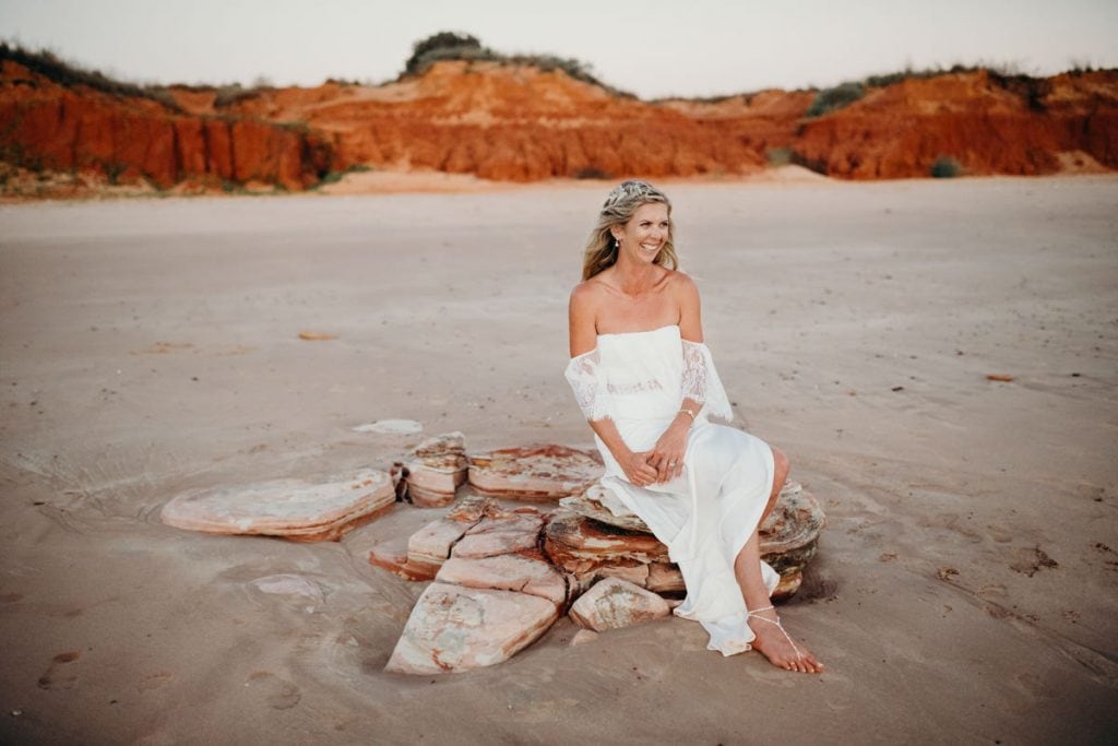 Broome bride sits on a rock on Riddell Beach in beautiful white wedding dress