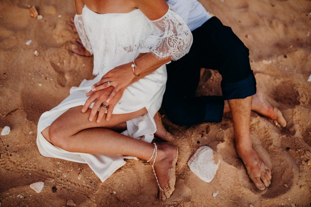 wedding couple sitting in the sand on the beach and holding hands