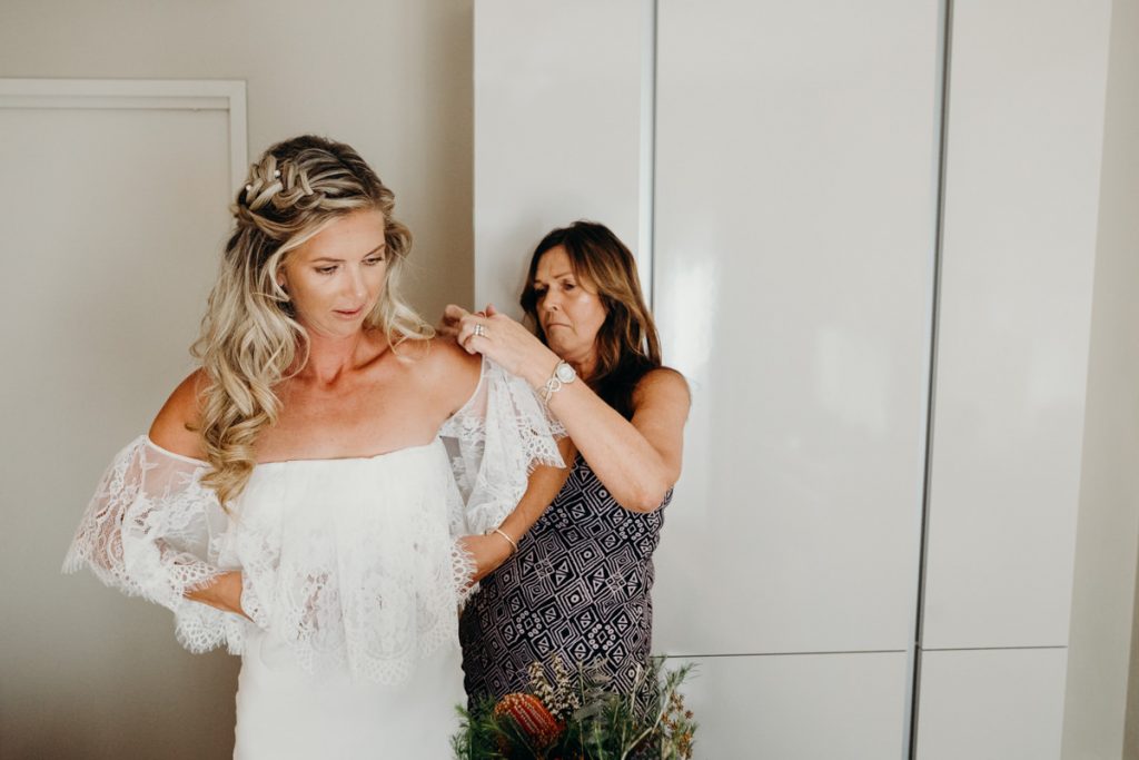 Mother of the bride is helping bride into wedding dress