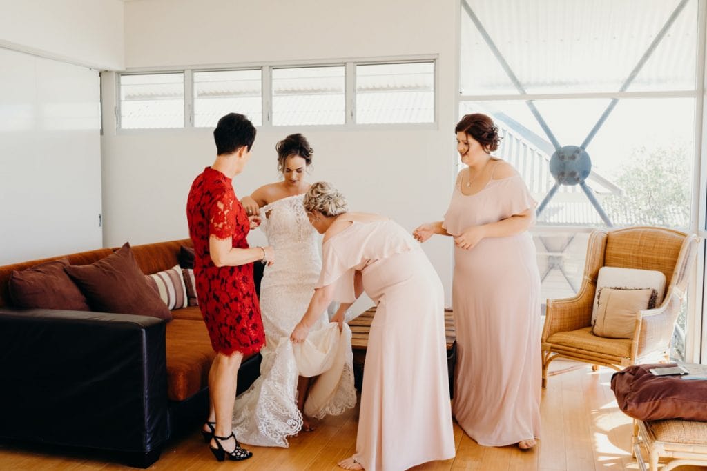 bride is getting help by bridesmaids and mother with getting into her wedding dress