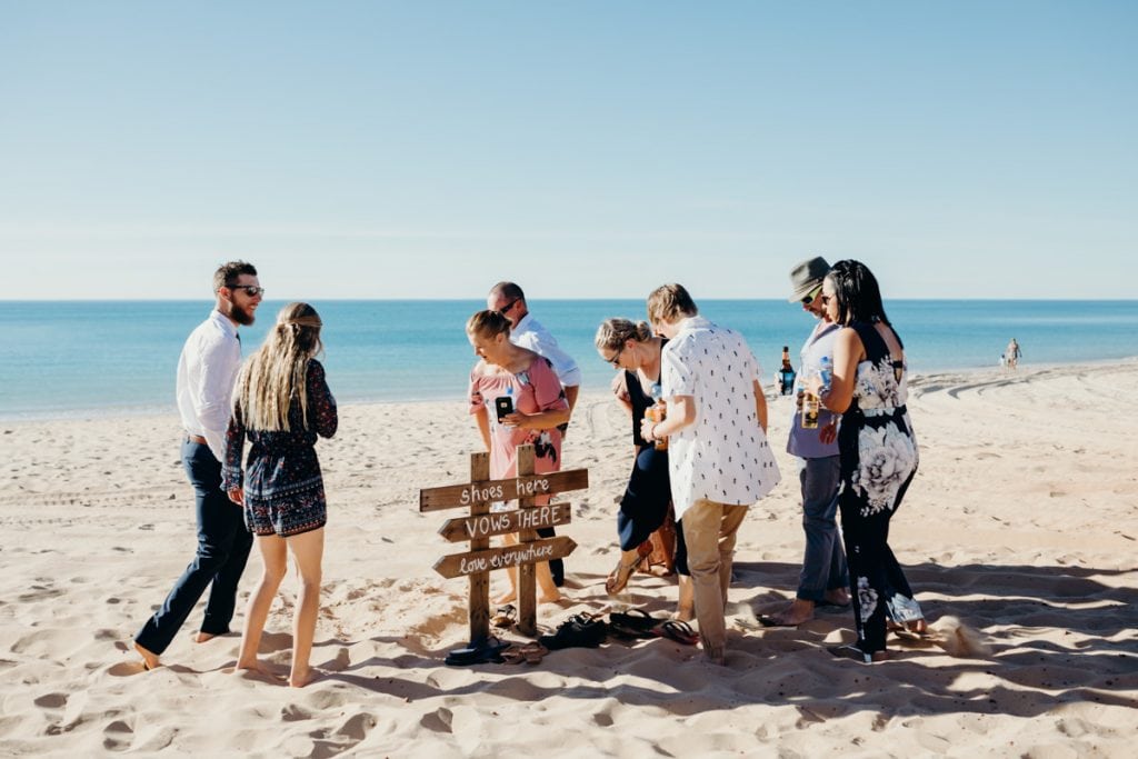wedding guests leaving shoes at wooden sign on the beach