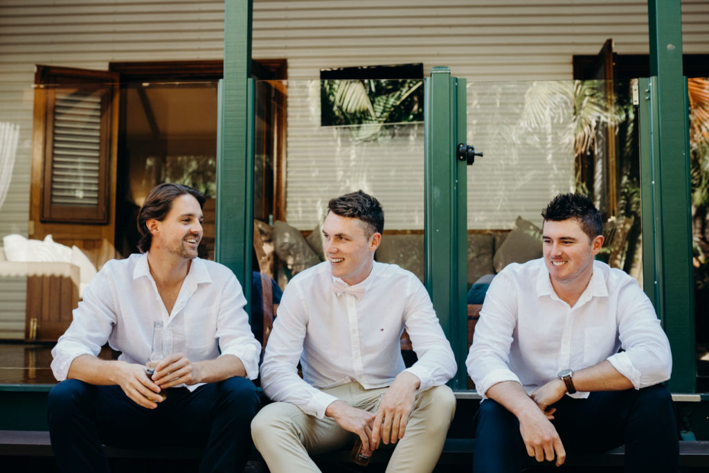 groom and two groomsmen sitting outside smiling at each other