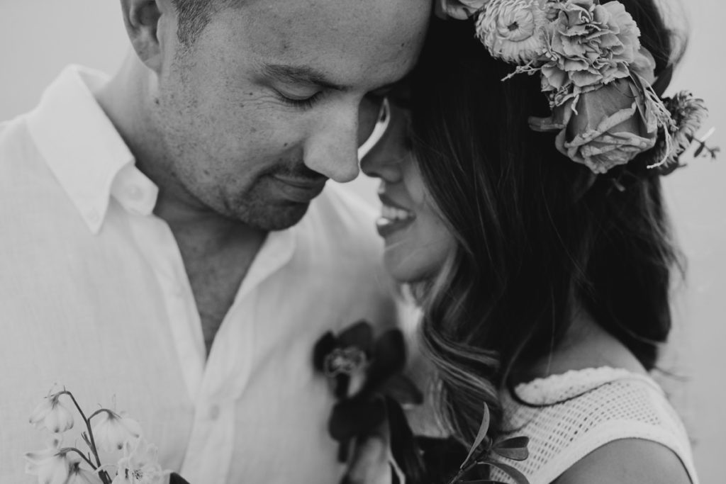 close up of bride and groom's faces with woman wearing a large flower crown 
