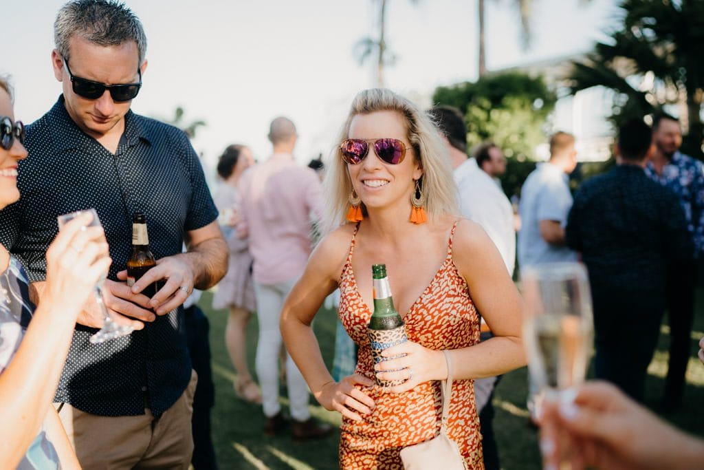 blonde woman in orange summer dress and beer in her hand at Broome wedding 