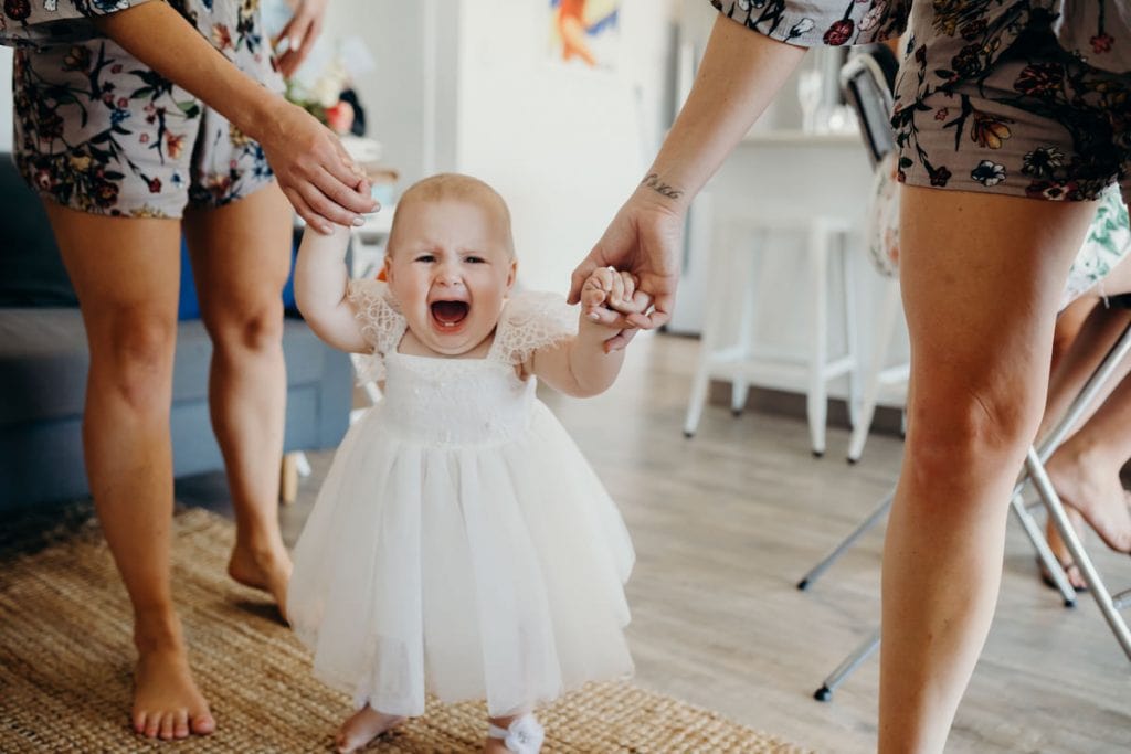 crying baby in white dress walking towards the bride
