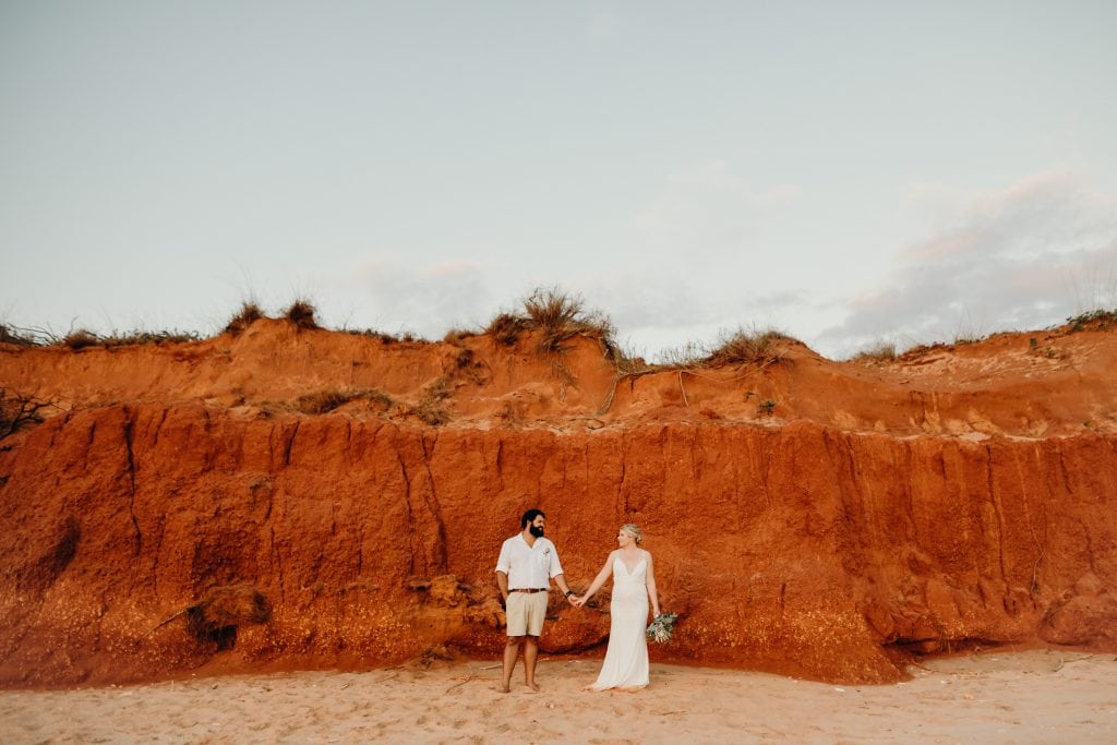 bride and groom holding hands standing in front of red cliff in Broome wedding photographer