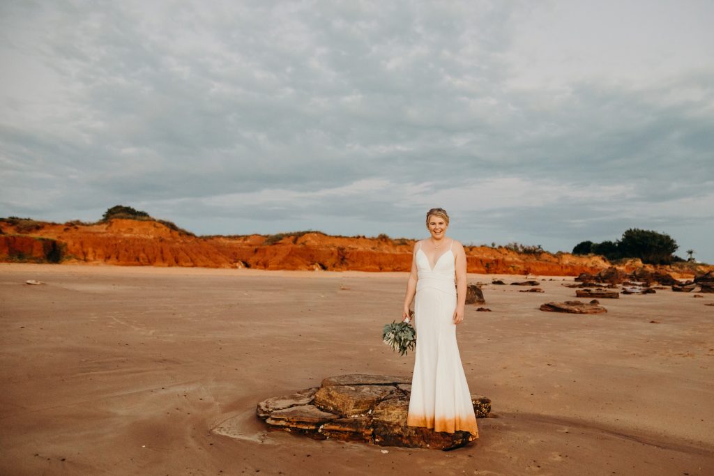 bride in white long wedding dress stand on a rock on the beach in Broome