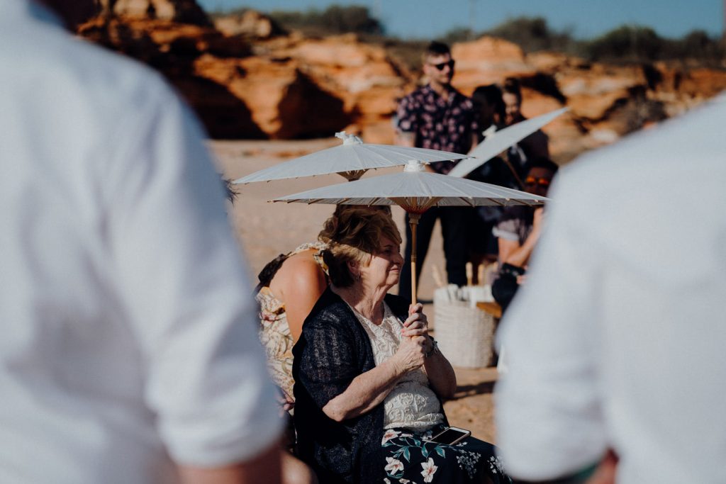 grandmother sitting on wooden bench at white parasol watching her granddaughter's ceremony