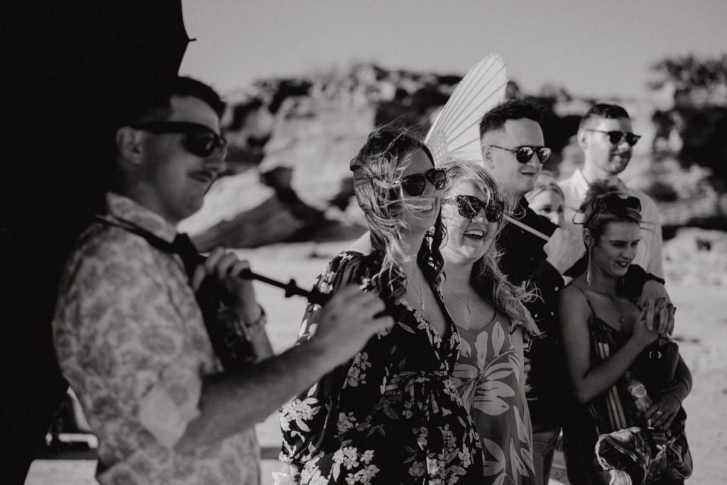 black and white photo of guests at beach wedding with hair flying in the wind and sun parasols