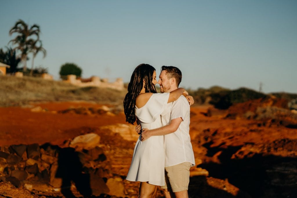 young engaged couple hugging each other with red rocks and palm trees in the background