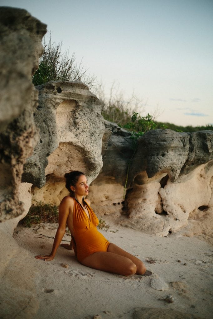woman in vintage bathing suit sitting in front of sandstone rocks
