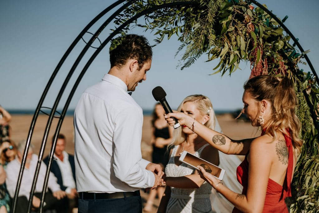 marriage celebrant Liz Quicke holding a microphone up to the groom during the wedding vows at Entrance Point wedding in Broome