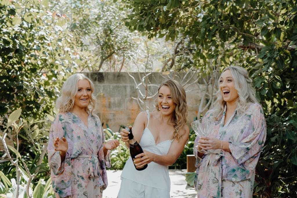 three young women laughing and popping champagne to celebrant Wedding at Gantheaume Point