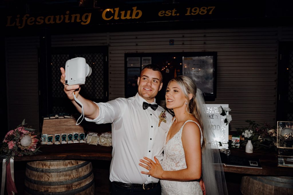 wedding couple taking a selfie with a polaroid camera at their relaxed beach wedding 