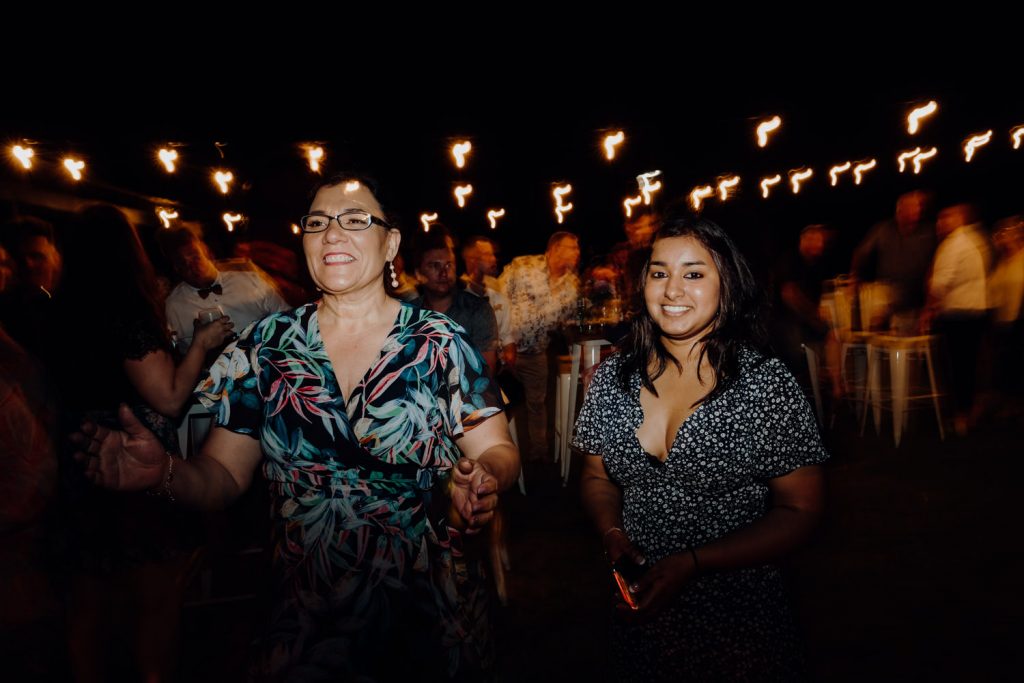 relaxed beach wedding reception with two women dancing under festoon lights