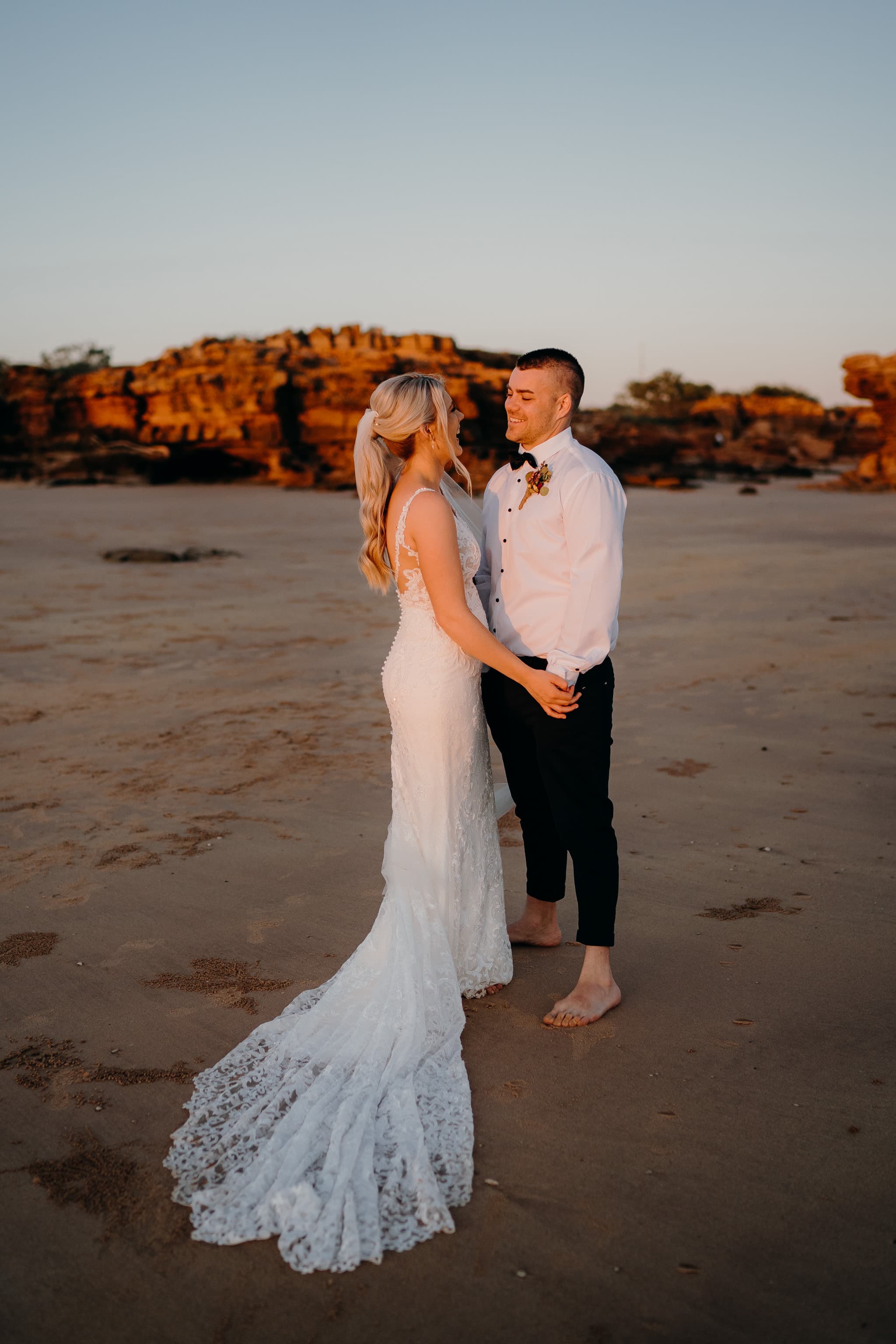 wedding couple holding hands looking at each other with red cliffs behind them